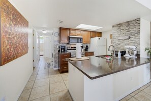 Une cuisine moderne dotée d’un îlot central, de meubles en bois, d’un four à micro-ondes et d’un réfrigérateur.