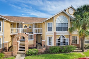 A two-story house with a covered front porch, a brick archway, and a palm tree in the yard. - Whimsical Wonders Sweetwater Club Near Disney (Kissimmee)