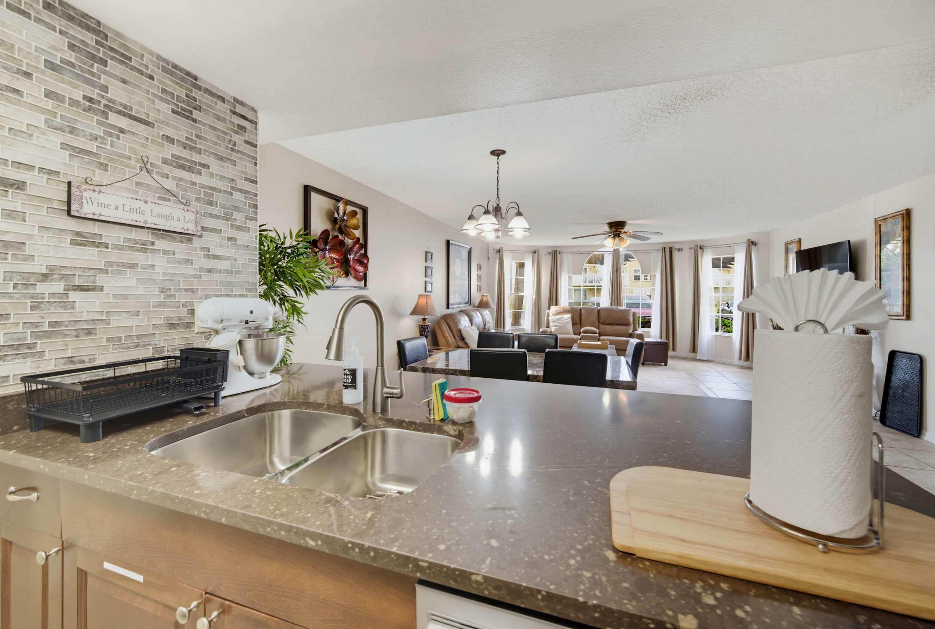 A modern kitchen with a granite countertop, stainless steel sink, and a dining area with a sofa and chairs.