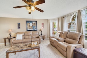 A living room with a ceiling fan, two sofas, a coffee table, and a large window with curtains. - Whimsical Wonders Sweetwater Club Near Disney (Kissimmee)