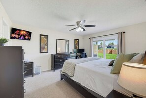 Une chambre à coucher comprenant un lit, une commode, un téléviseur, un ventilateur de plafond et une fenêtre donnant sur l’extérieur.