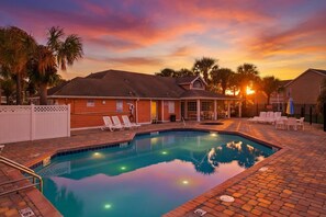 A swimming pool with lounge chairs, a covered area, and a sunset in the background. - Whimsical Wonders Sweetwater Club Near Disney (Kissimmee)