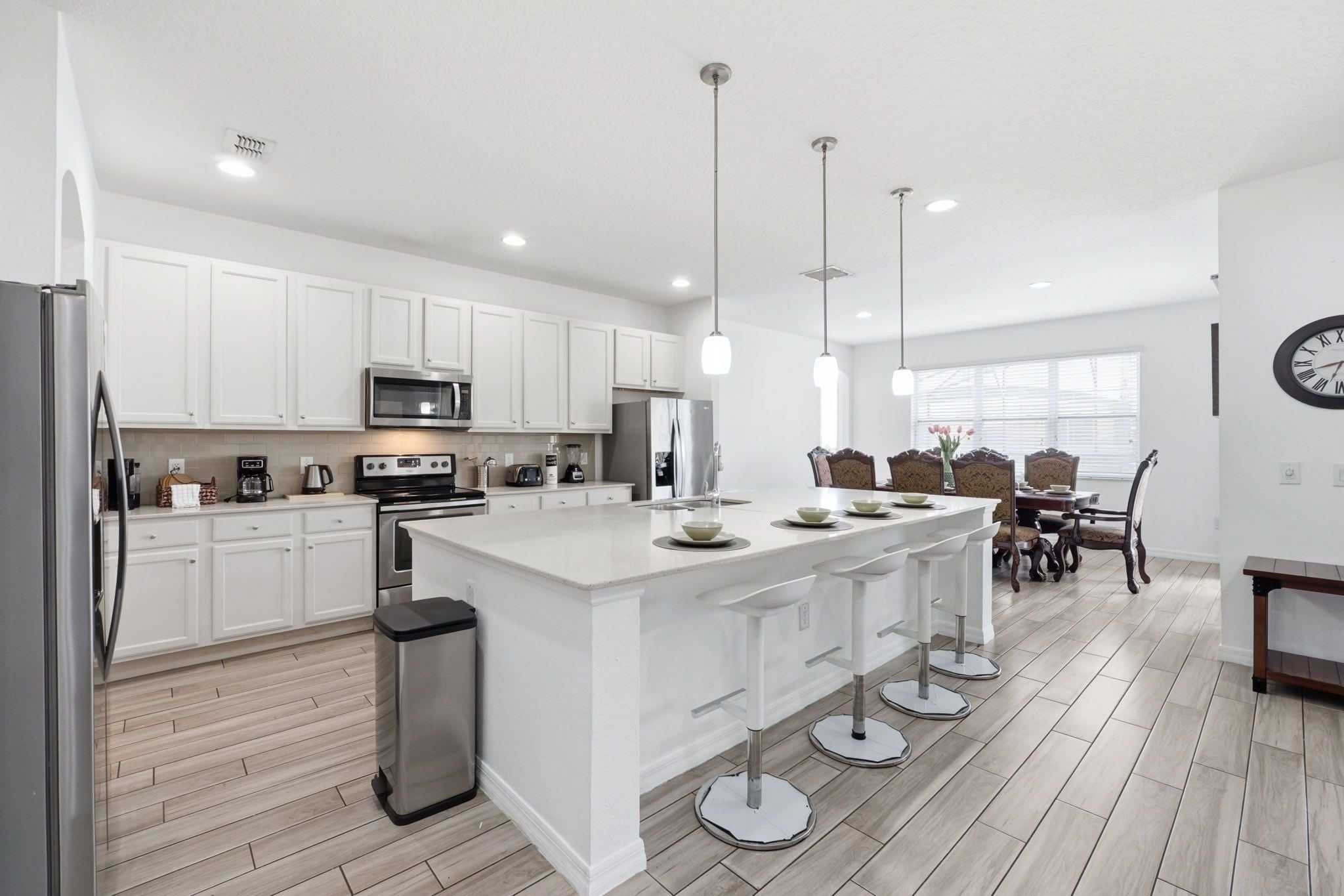 A modern kitchen with white cabinetry, stainless steel appliances, and a central island with bar stools.