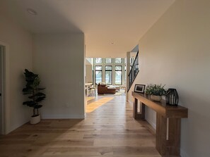A hallway with wooden flooring leading to a living area with a sofa, a dining table, and large windows. - Modern 4 bedroom Lakehouse on Alexandria chain of lakes! (Alexandria)