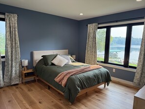 Ein Schlafzimmer mit einem Bett, einem Nachttisch, einer Lampe und einem Fenster mit Seeblick.