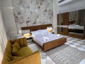 Un dormitorio moderno con una cama grande, una mesita de noche, una silla, un espejo y una alfombra estampada.