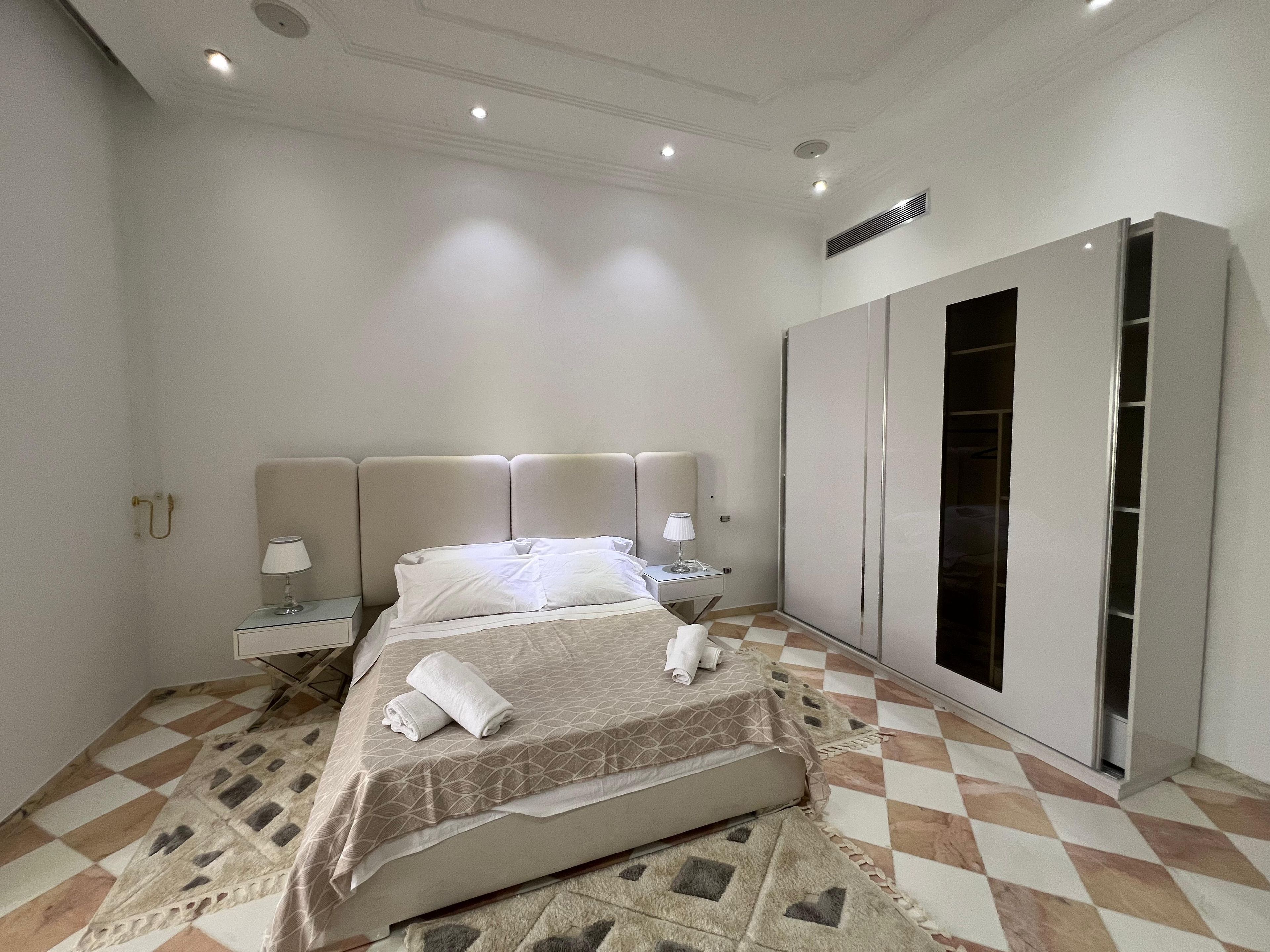 Una habitación de hotel con cama, lámparas de noche, armario y suelo estampado.