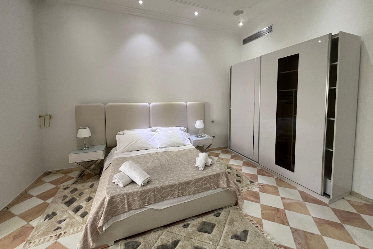 Une chambre d’hôtel avec un lit, des lampes de chevet, une armoire et un sol à motifs.