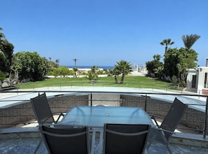 Un espace extérieur aménagé avec une table et des chaises, offrant une vue sur un jardin paysager et la mer.