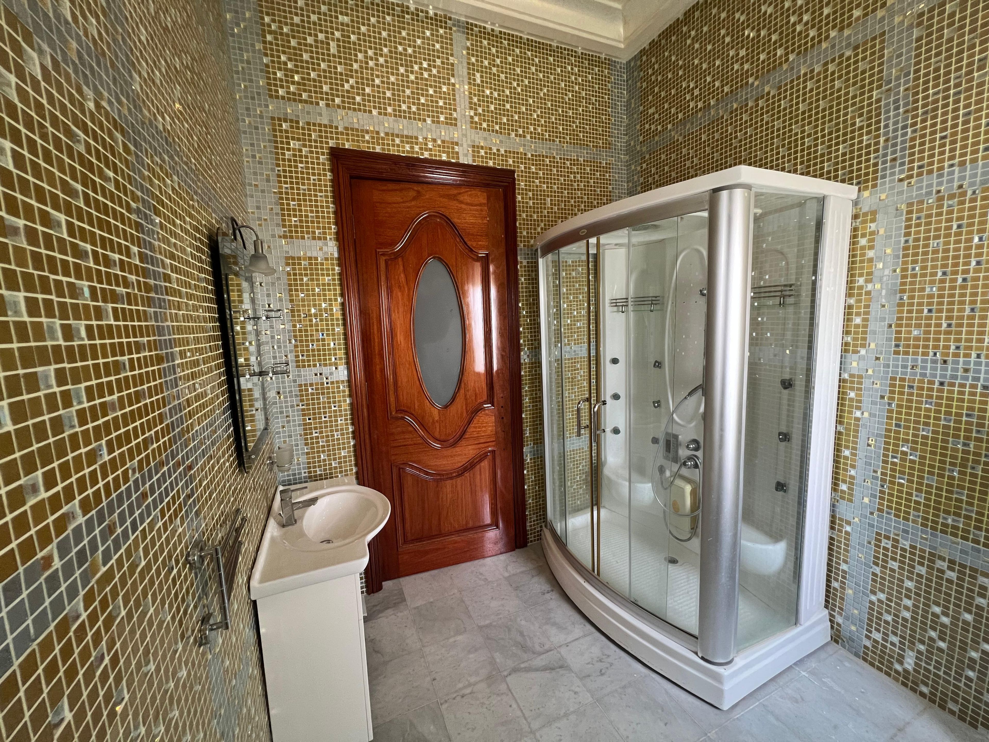 A bathroom with a wooden door, a glass-enclosed shower, and a sink.