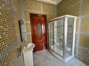 Une salle de bain avec une porte en bois, une douche fermée par des parois de verre et un lavabo.