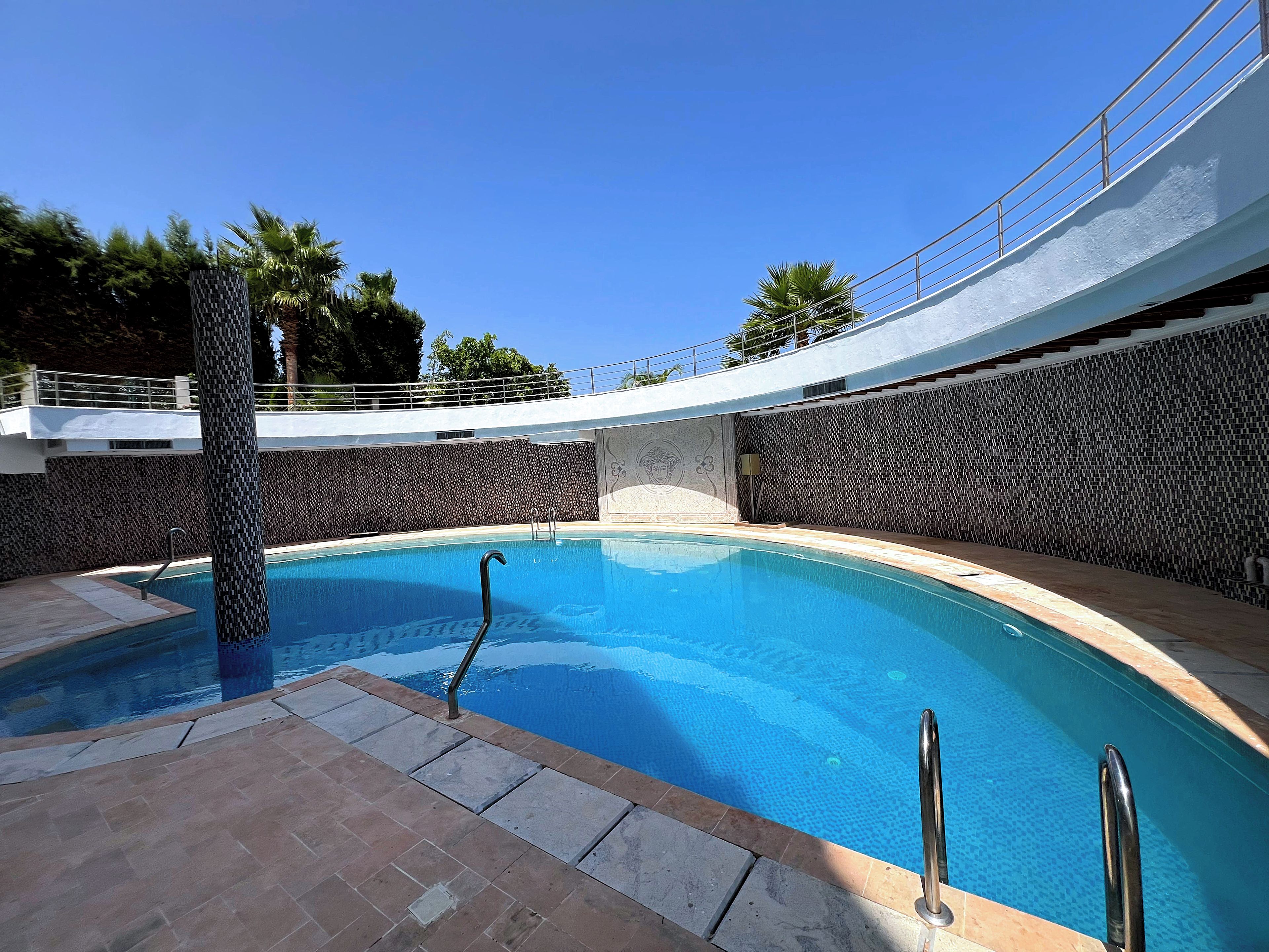 Ein Schwimmbecken mit Fliesen umrandet, einem Metallgeländer und einer Wand mit Mosaikdekor.