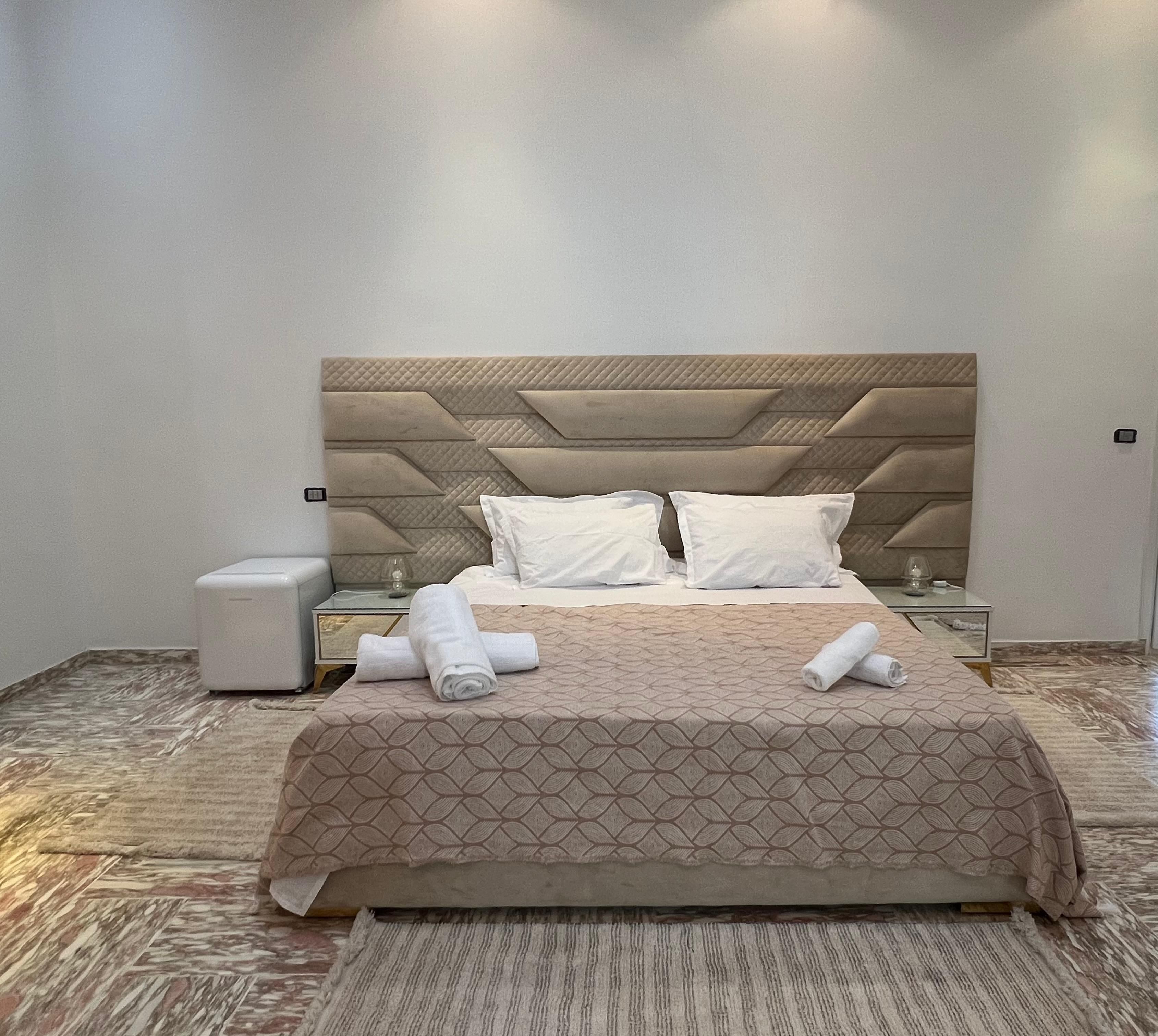 Ein ordentlich gemachtes Bett mit einer gemusterten Tagesdecke, zwei Kissen und aufgerollten Handtüchern auf einem Holzboden mit Teppich.