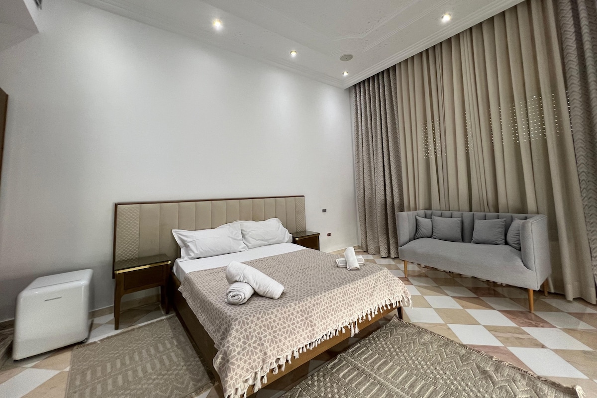 Une chambre à coucher moderne avec un lit, un canapé, une table de chevet et une lampe sur pied.