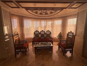 Una habitación con una mesa central, dos sillas ornamentadas y una lámpara decorativa.