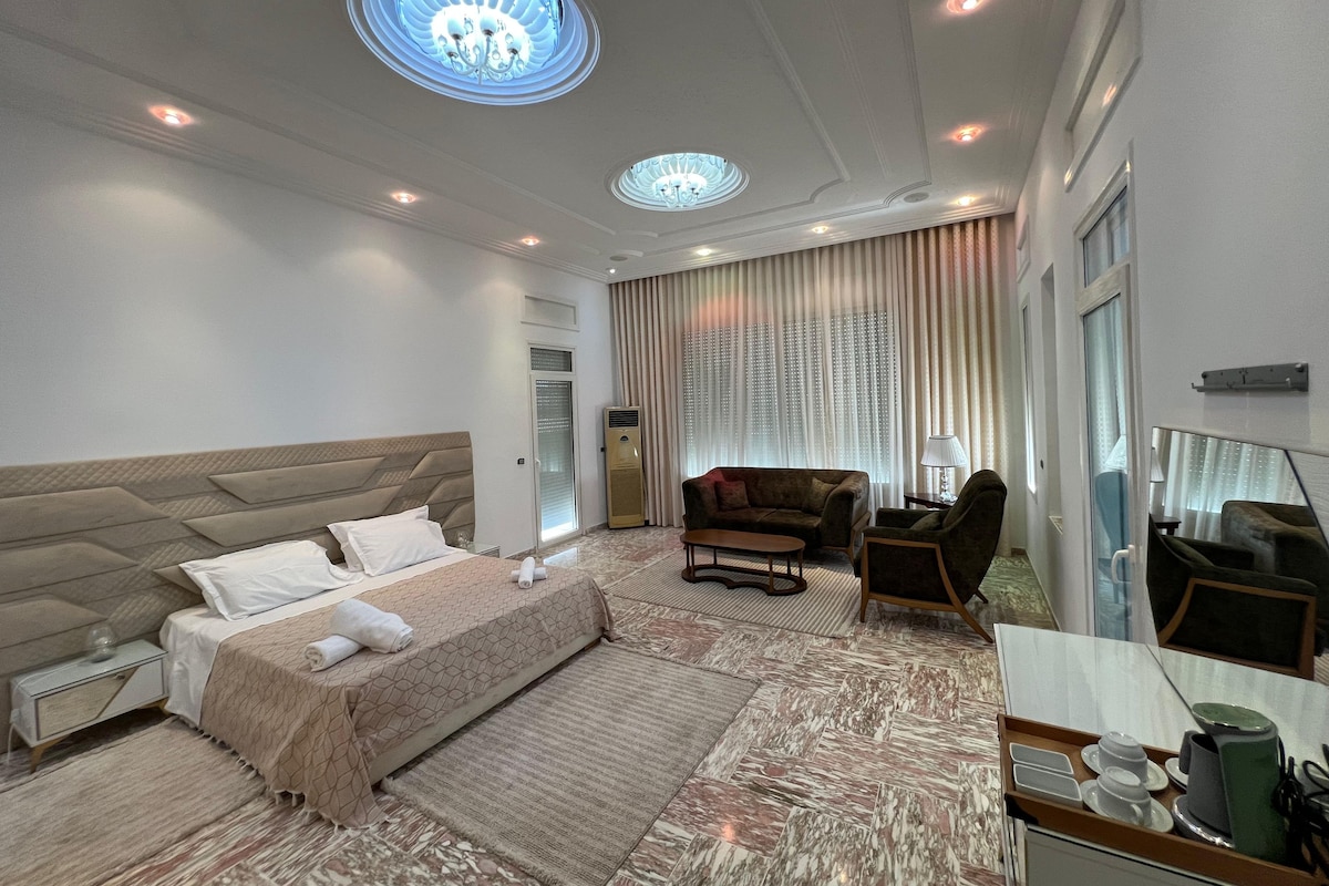 Une chambre d’hôtel avec un grand lit, un canapé, un bureau avec un miroir et un lustre.
