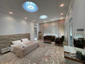 Une chambre d’hôtel avec un grand lit, un canapé, un bureau avec un miroir et un lustre.