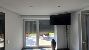 Quarto com porta de vidro deslizante para um pátio externo, televisão de tela plana na parede e um vaso grande no chão.