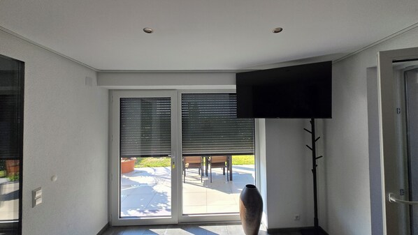 A room with a sliding glass door leading to an outdoor patio, a flat-screen TV mounted on the wall, and a large vase on the floor.