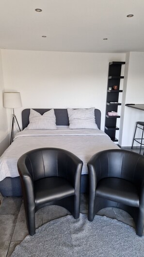 Quarto moderno com uma cama grande, duas poltronas de couro preto, uma escrivaninha com cadeira e uma luminária.