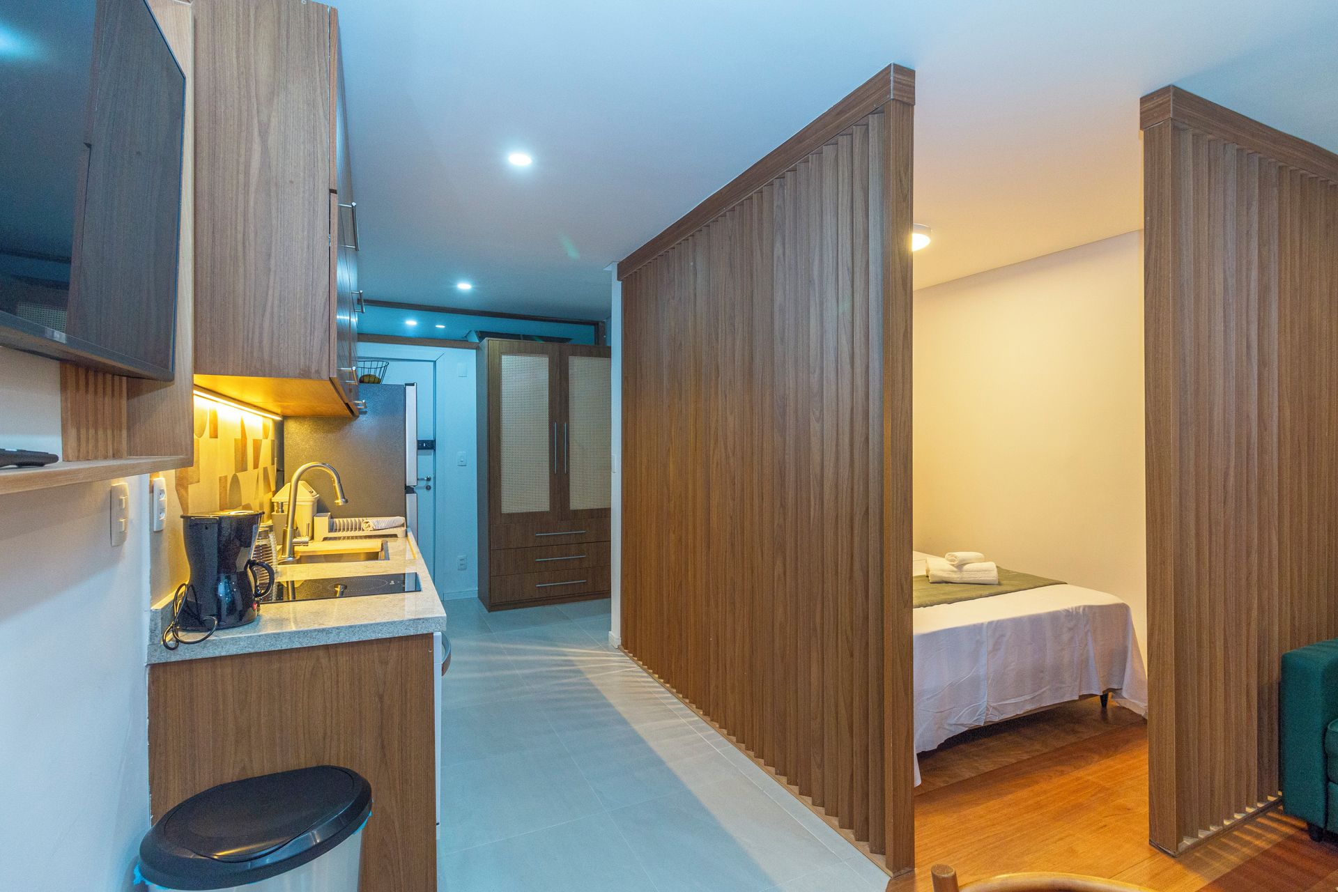 Een kleine kamer met een kitchenette, een bed en een badkamer.