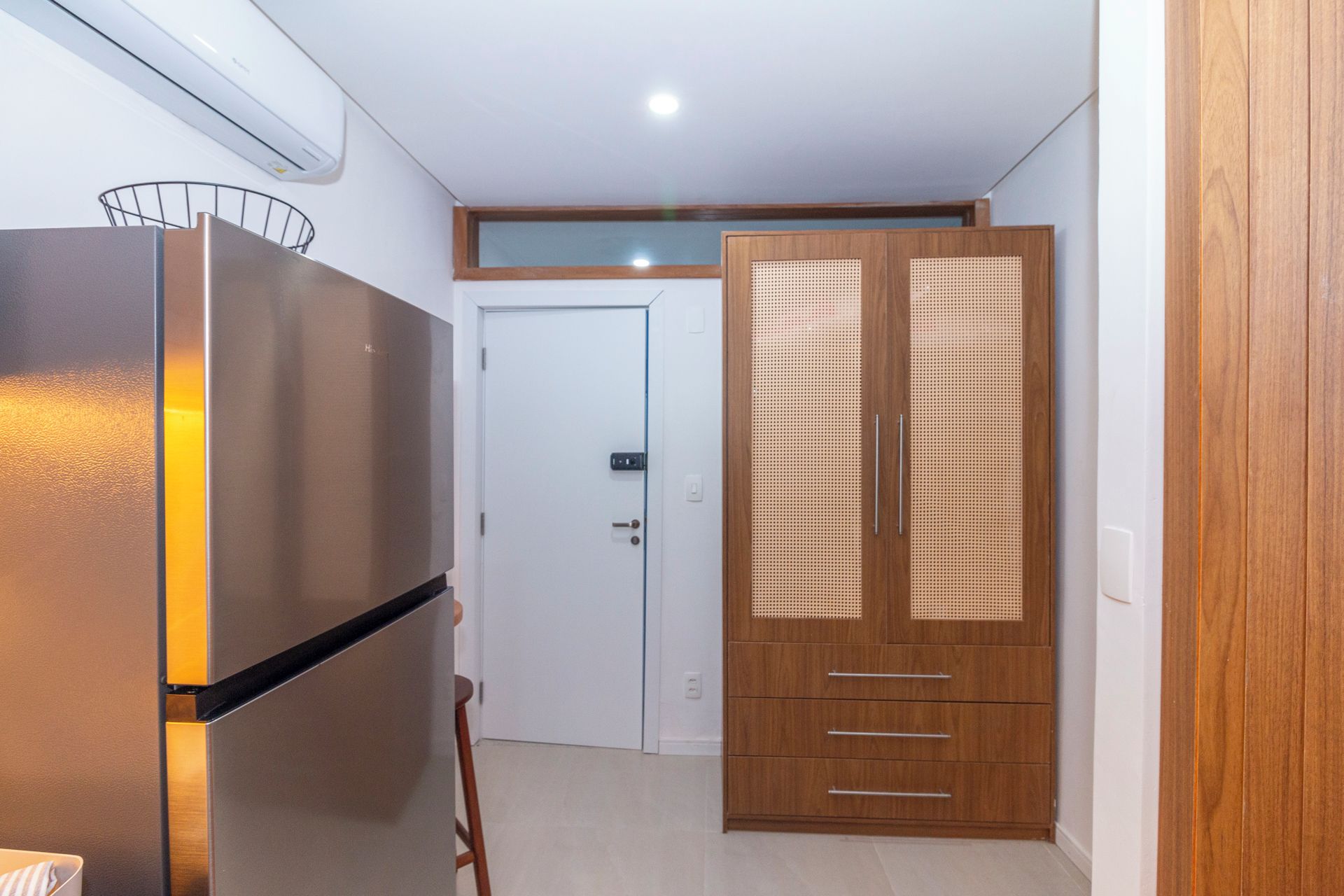 Een kamer met een geïntegreerde koelkast, een witte deur en een houten garderobe met een geweven paneel.