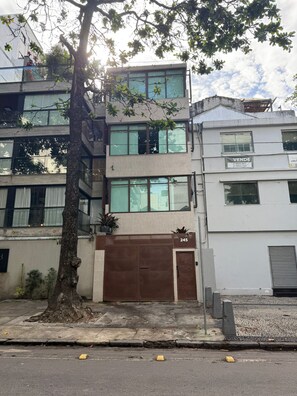 Un edificio de varios pisos con un árbol grande al frente, una puerta de garaje y un letrero que anuncia una venta.