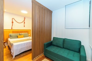 Una habitación con una cama, un sofá verde, un separador de madera y una pizarra en la pared.