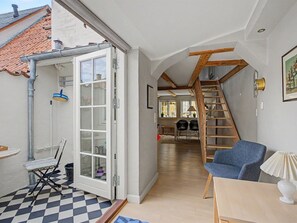 Une pièce spacieuse avec un sol à carreaux, une chaise bleue, une table en bois et un escalier menant à un niveau supérieur.