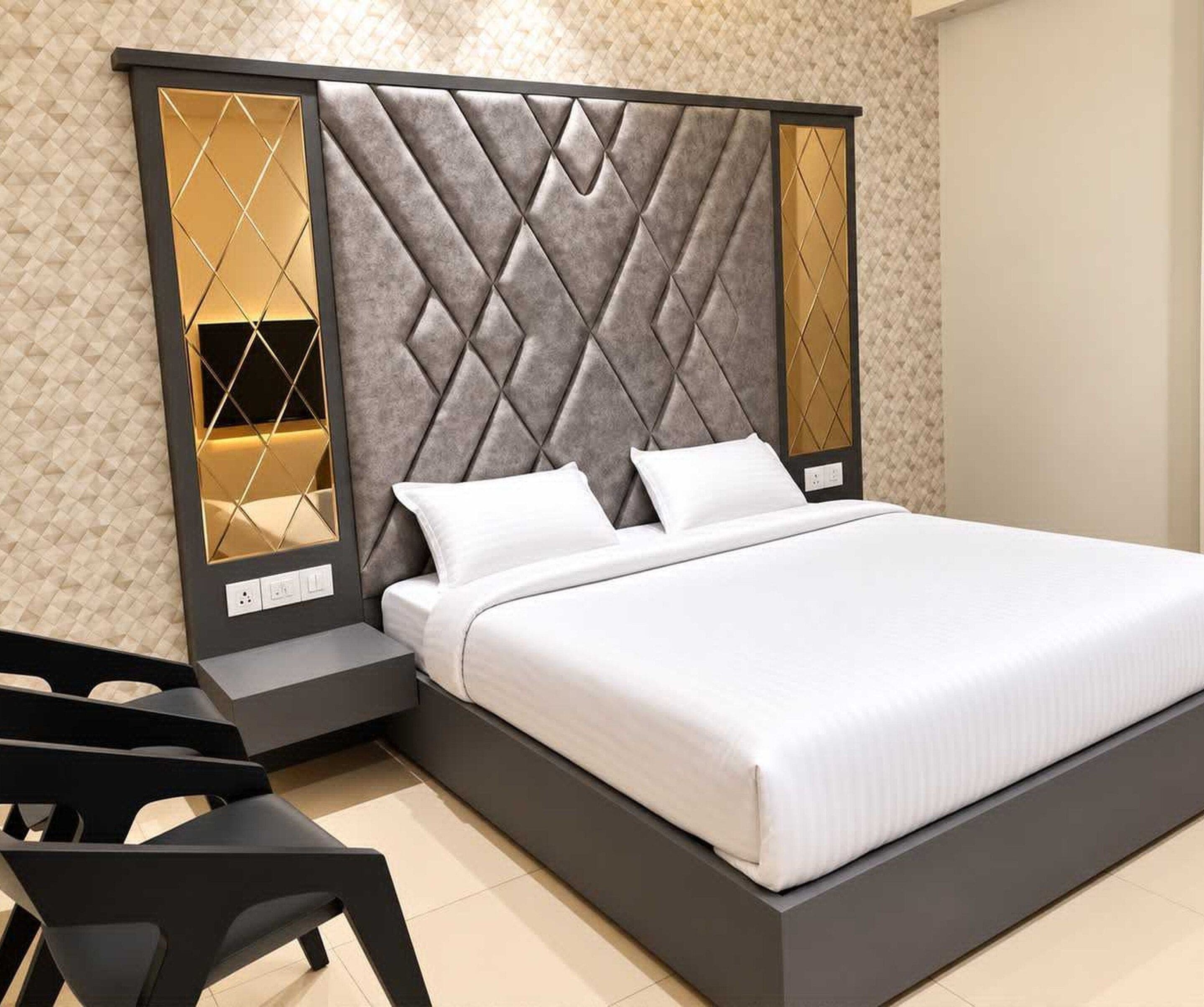 A modern bed with a grey upholstered headboard and white bedding, a small bedside table, and a chair.