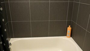 A bathtub with a shower curtain, a bottle of shampoo, and dark tiled walls. - Delightful 1BR Apt in Ravenswood (Chicago)