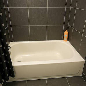 A bathtub with a shower curtain, a bottle of shampoo, and dark tiled walls. - Delightful 1BR Apt in Ravenswood (Chicago)