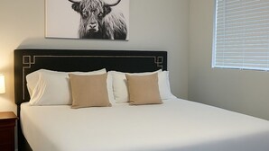 A neatly made bed with a headboard, a bedside table, and a wall-mounted artwork of a bull. - Delightful 1BR Apt in Ravenswood (Chicago)