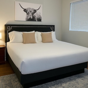 A neatly made bed with a headboard, a bedside table, and a wall-mounted artwork of a bull. - Delightful 1BR Apt in Ravenswood (Chicago)