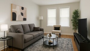 Un salon comprenant un canapé, une table basse, un meuble pour la télévision, une lampe et une plante.