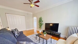 Una sala de estar con sofá, sillón, mesa de centro, televisor y ventilador de techo.