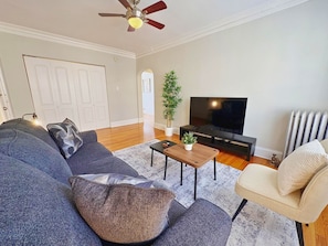 A living room with a sofa, armchair, coffee table, TV, and a ceiling fan. - Homey Vibes 1BR Apt near Lake Michigan & UChicago (Chicago)