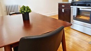 Una mesa de comedor con una silla, una planta en maceta y una cocina con armarios y un horno al fondo.