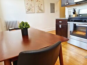 A dining table with a chair, a potted plant, and a kitchen with cabinets and an oven in the background. - Homey Vibes 1BR Apt near Lake Michigan & UChicago (Chicago)