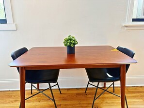 A rectangular wooden table with four black chairs, a small potted plant on the table, and a window with blinds in the background.