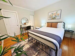 A bedroom with a bed, bedside table, lamp, and a painting on the wall.