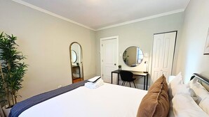 Una habitación de hotel con cama, escritorio, silla, espejo y una planta en maceta.
