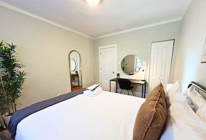 A hotel room with a bed, a desk, a chair, a mirror, and a potted plant. - Homey Vibes 1BR Apt near Lake Michigan & UChicago (Chicago)