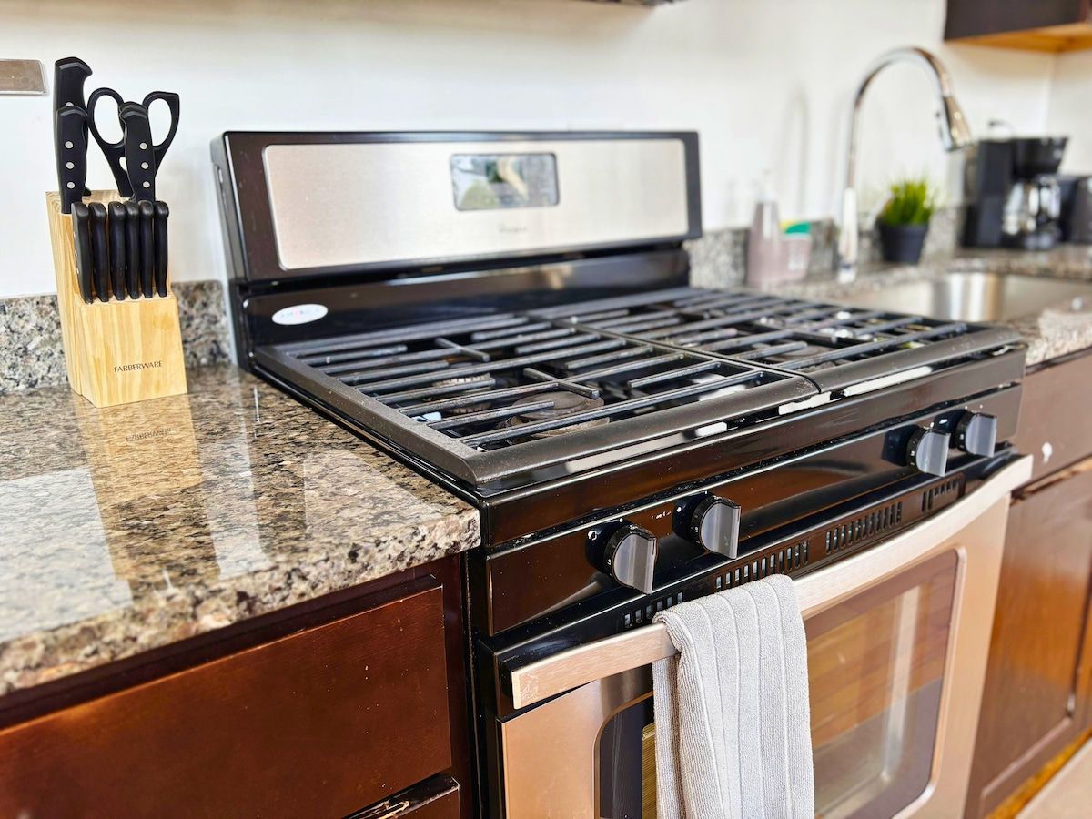 A kitchen with a stainless steel stove, a wooden utensil holder, and a granite countertop.