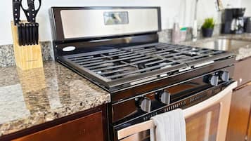 A kitchen with a stainless steel stove, a wooden utensil holder, and a granite countertop.