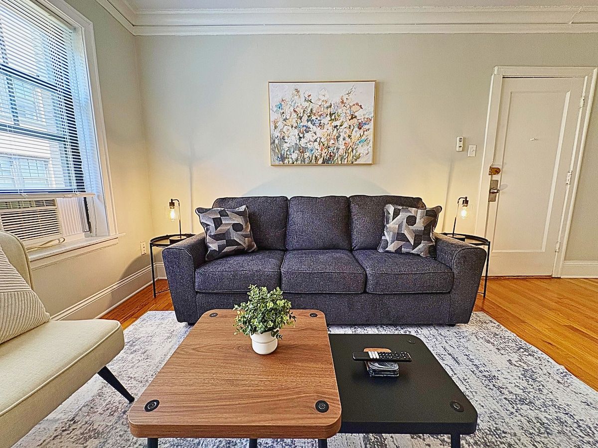 A living room with a sofa, a coffee table with a plant, and a painting on the wall.