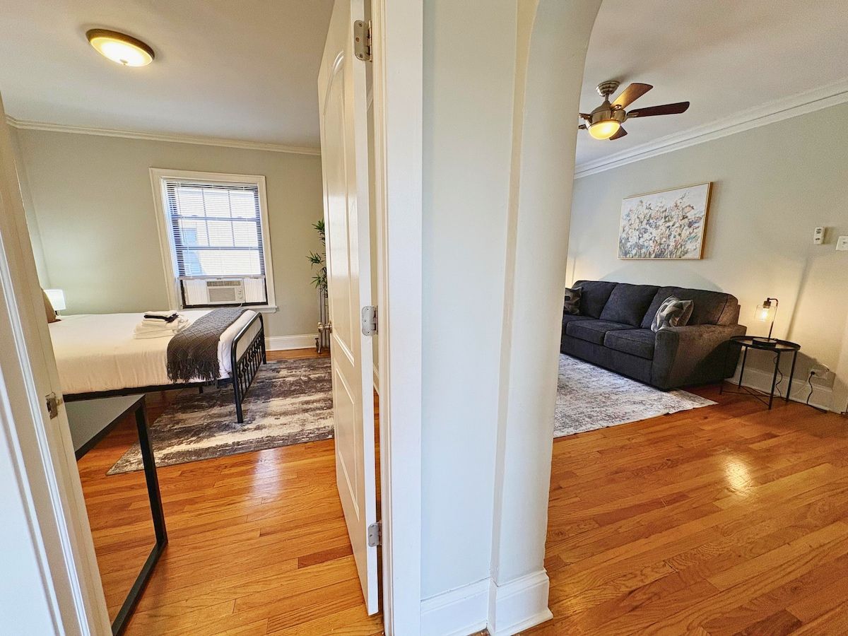 A room with a bed, a window, a radiator, a ceiling fan, and a couch.