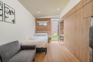 A modern bedroom with a bed, a grey sofa, a wooden wardrobe, and a small balcony with a chair. - Apto Moderno 1Hab Bogota Terraza Sierra Madre 109 (Bogotá)