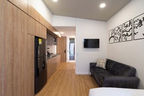 Een moderne keuken met houten kastjes, een zwarte koelkast en een flatscreen televisie aan de wand.