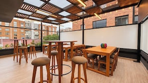 Een modern interieur met houten tafels en krukken, grote ramen en uitzicht op gebouwen.